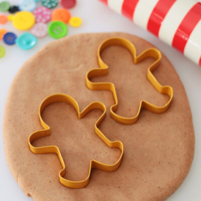 two gingerbread man cookie cutters with play dough, rolling pin and buttons