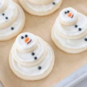 Snowman cookies on baking sheet with brown parchment paper.