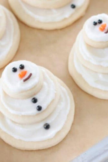 Snowman cookies on baking sheet with brown parchment paper.