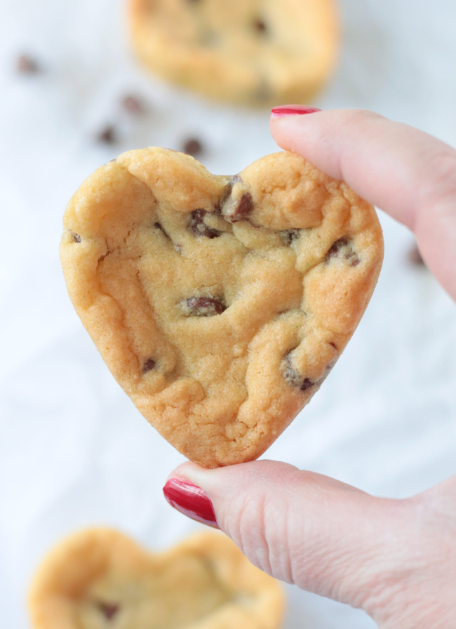 hand holding heart shaped chocolate chip cookie