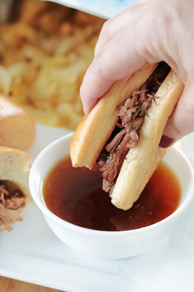 hand dipping slow cooker French dip into au jus