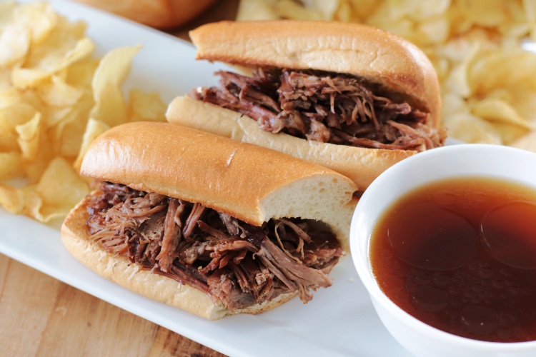 French dip sandwich with potato chips and au jus on platter