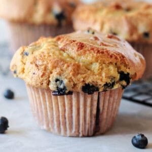 Jumbo bakery style blueberry muffin next to cooling rack of muffins.
