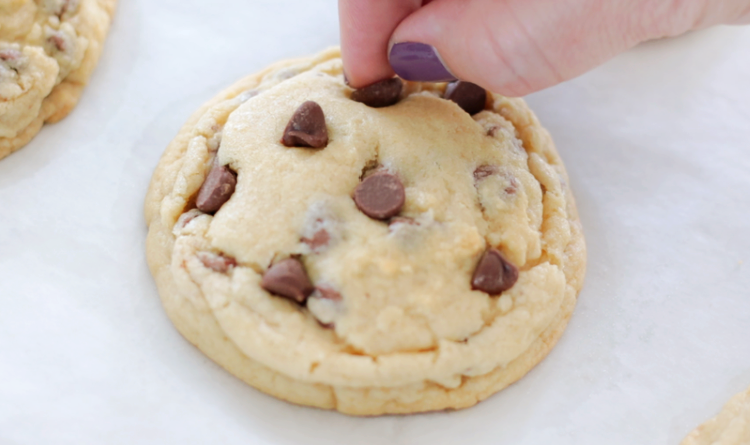 hand adding additional chocolate chips onto the top of the baked cookie