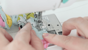 hand holding fabric as it is sewn in sewing machine