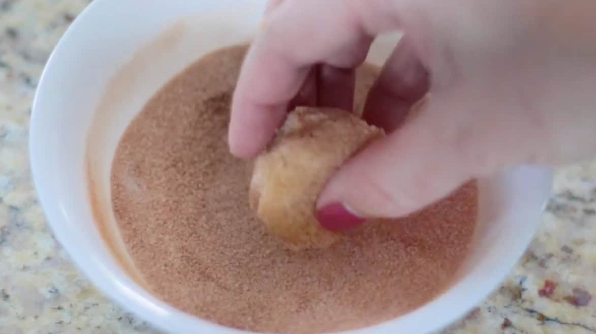 Hand rolling balls of cookie dough in bowl of cinnamon and sugar.