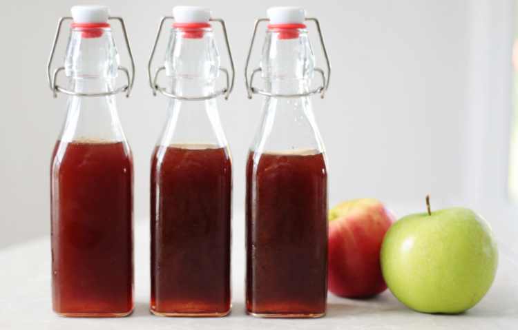 3 bottles of boiled apple cider with apples on a table