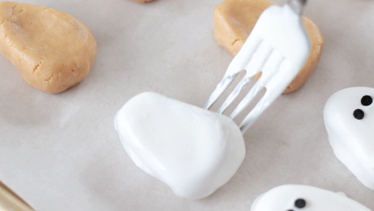 fork sliding peanut butter ghost onto baking sheet