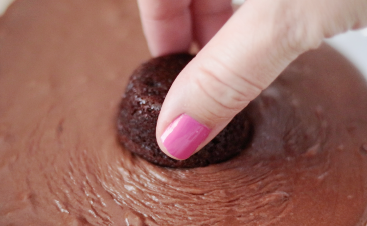 hand dipping cake bite into melted chocolate frosting