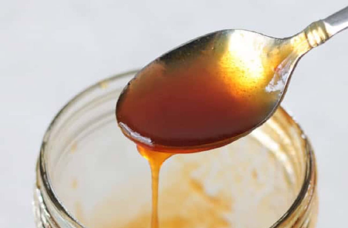 Spoonful of boiled cider syrup dripping into jar.