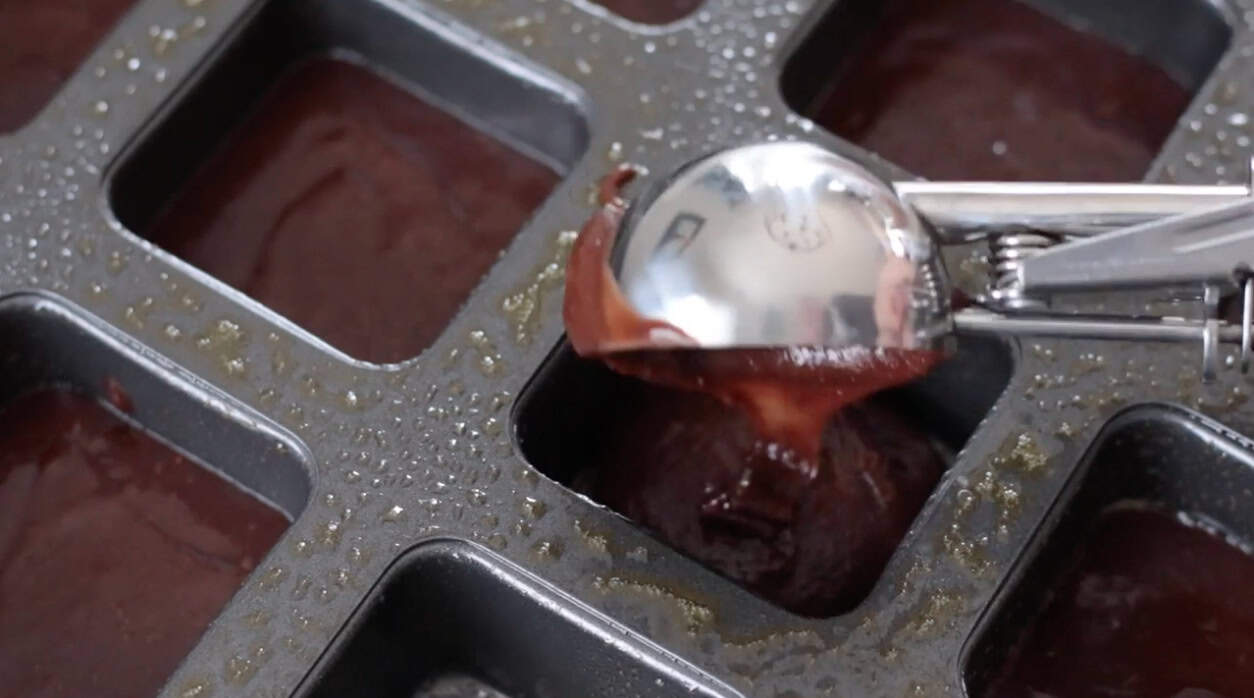 Brownie batter scooped into square brownie baking pan.