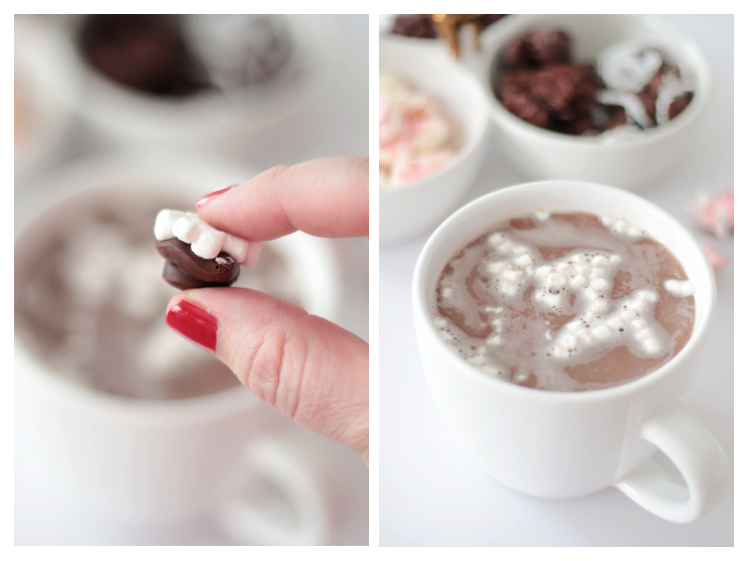 hand holding chocolate candy with mini marshmallows and cup of hot chocolate