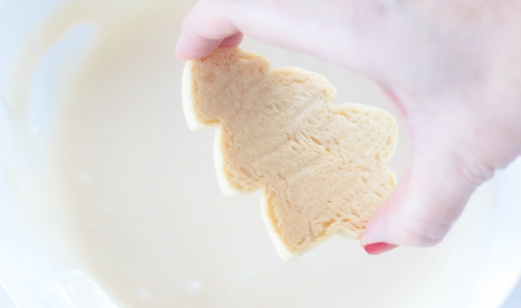 hand dipping sugar cookie into frosting