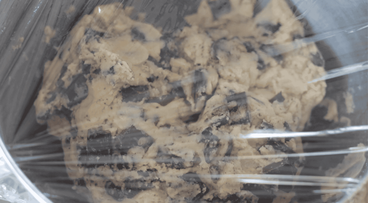 Bowl of cookie dough covered with plastic wrap.