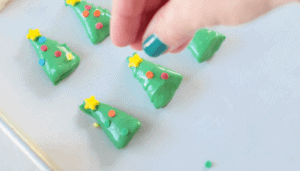 hand sprinkling colored sprinkles on green dipped bugles