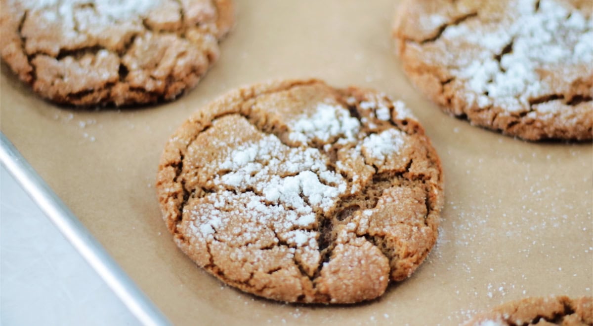 Baked molasses cookies on baking sheet with parchment paper.