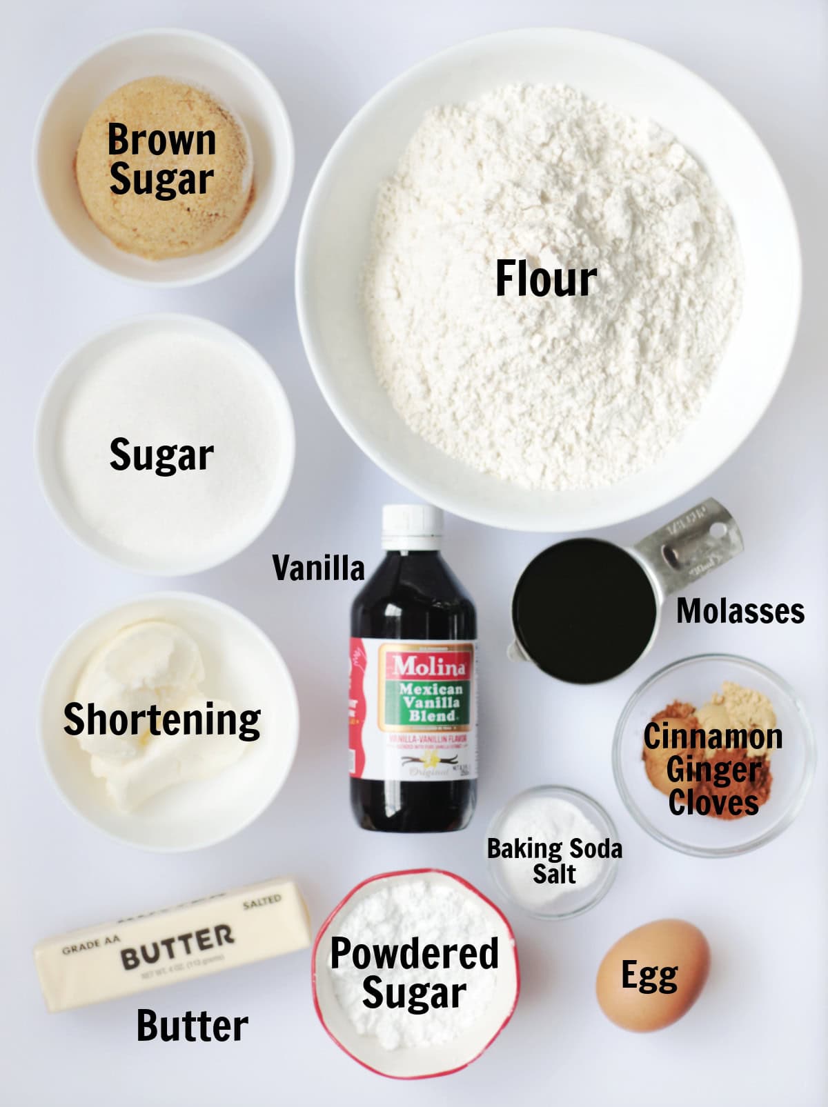 Bowls of brown sugar, sugar, shortening, stick of butter, bowls of flour, powdered sugar, spices, baking soda and salt, stick of butter, bottle of vanilla and an egg.