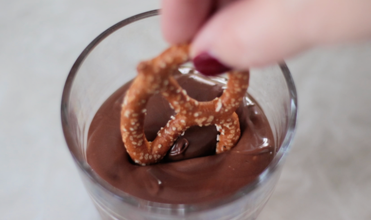 hand dipping pretzel into chocolate