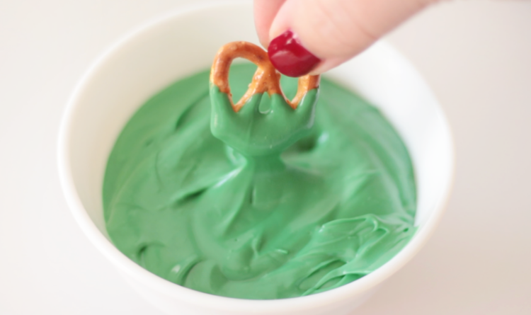 hand dipping a mini pretzel in green melting chocoalte