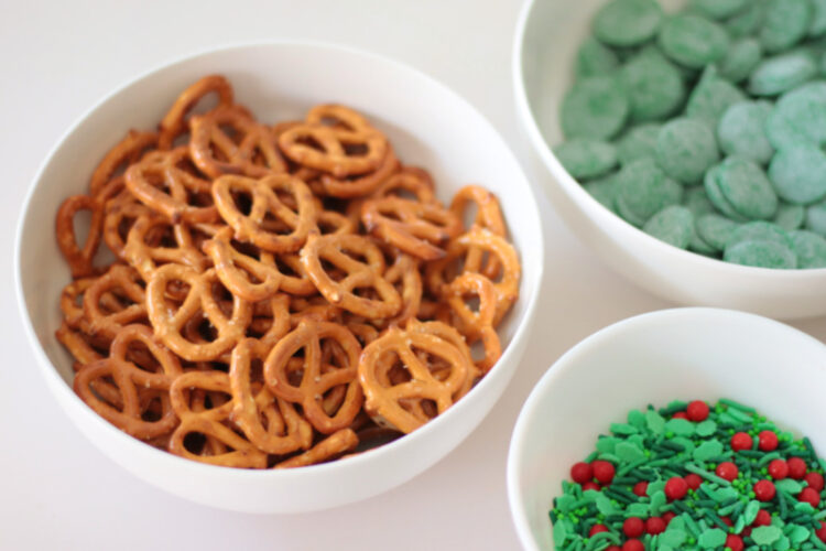 bowl of mini pretzels, bowl of green melting wafers and bowl of holiday sprinkles