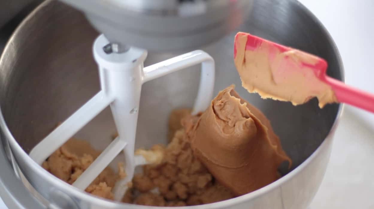Peanut butter on spatula added to bowl of a stand mixer.