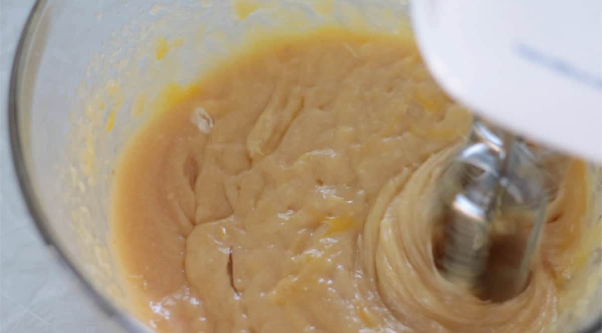 Electric mixer beating sugar, eggs and butter in glass mixing bowl.