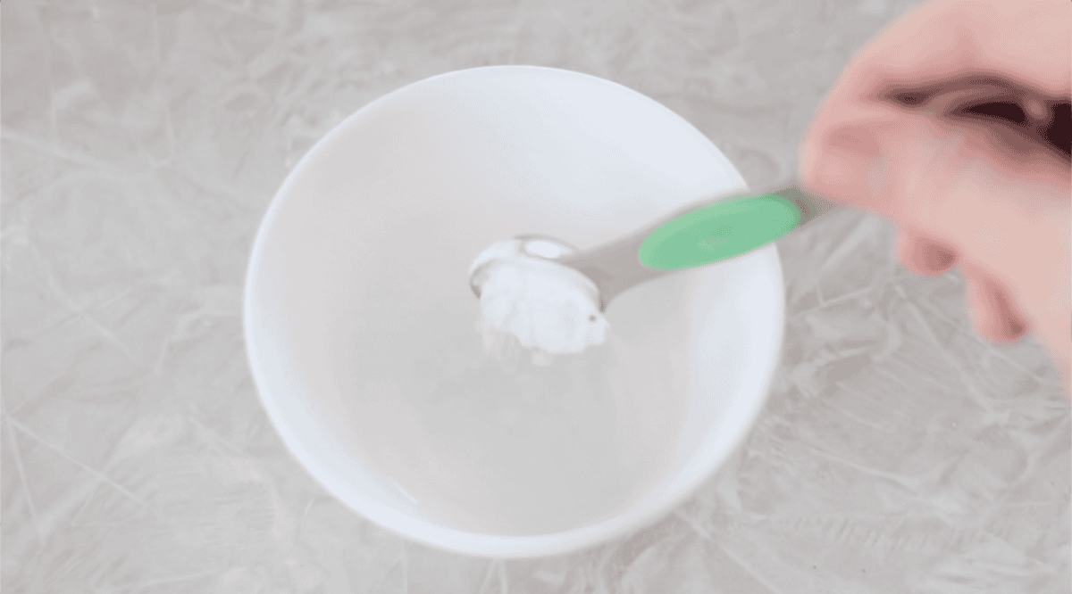 Small white bowl of water and teaspoon of baking soda.