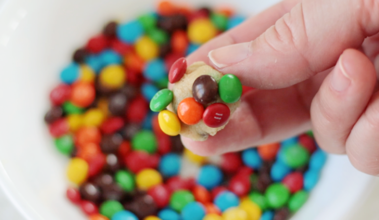 hand holding tiny piece of cookie dough dipped in candies