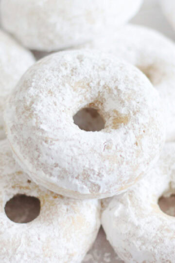 Powdered sugar donuts stacked on top of eachother.