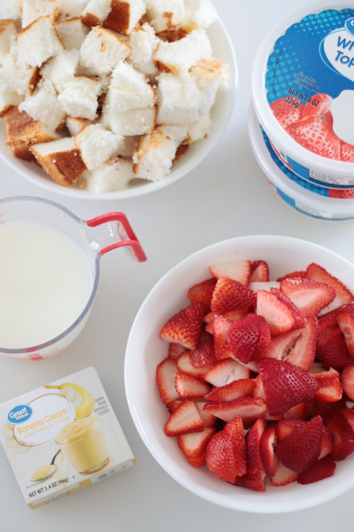 bowls of cake, sliced strawberries and milk with box of banana pudding and two containers of whipped cream