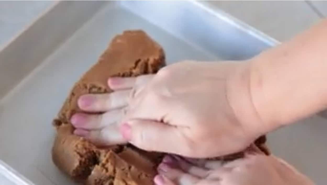 Hands pressing gingerbread cookie dough into baking pan.