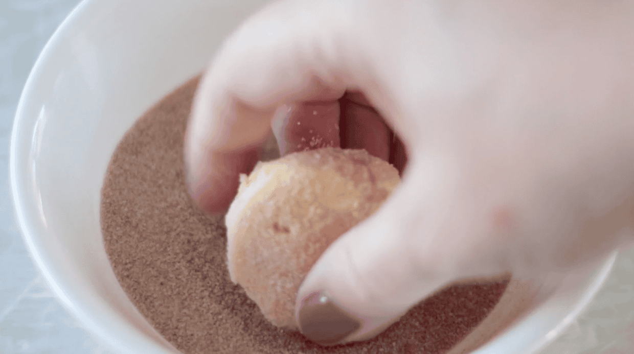 Close-up of hand dipping a cookie into cinnamon sugar for snickerdoodles.