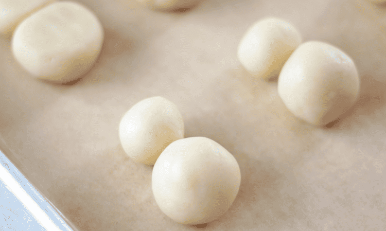 Balls of cookie dough on baking sheet with parchment paper.