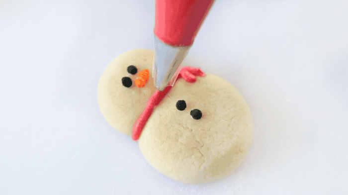 Piping a red scarf onto a snowman sugar cookies.