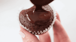 spoon pouring small amount of ganache over cupcake