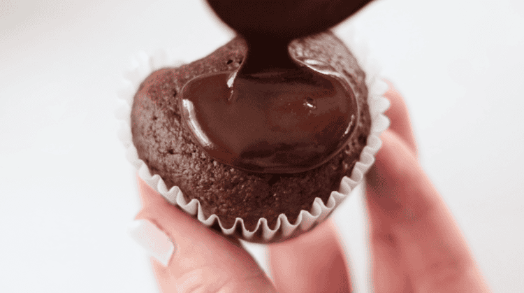 spoon pouring small amount of ganache over cupcake