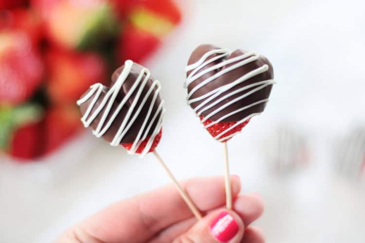 hand holding two chocolate strawberry hearts