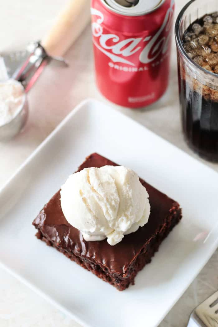 white plate with slice of coca cola chocolate cake and scoop of ice cream