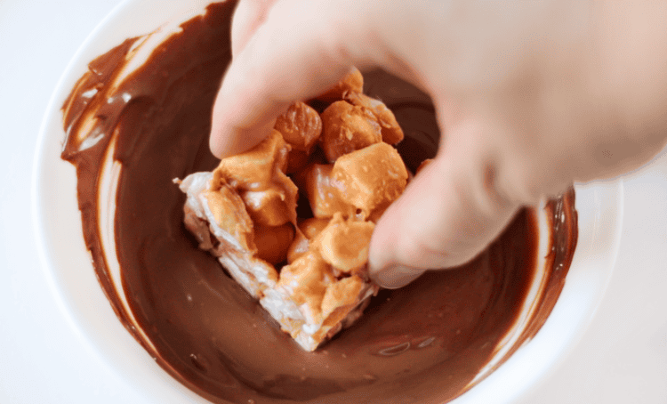 hand dipping peanut butter marshmallow square into melted chocolate