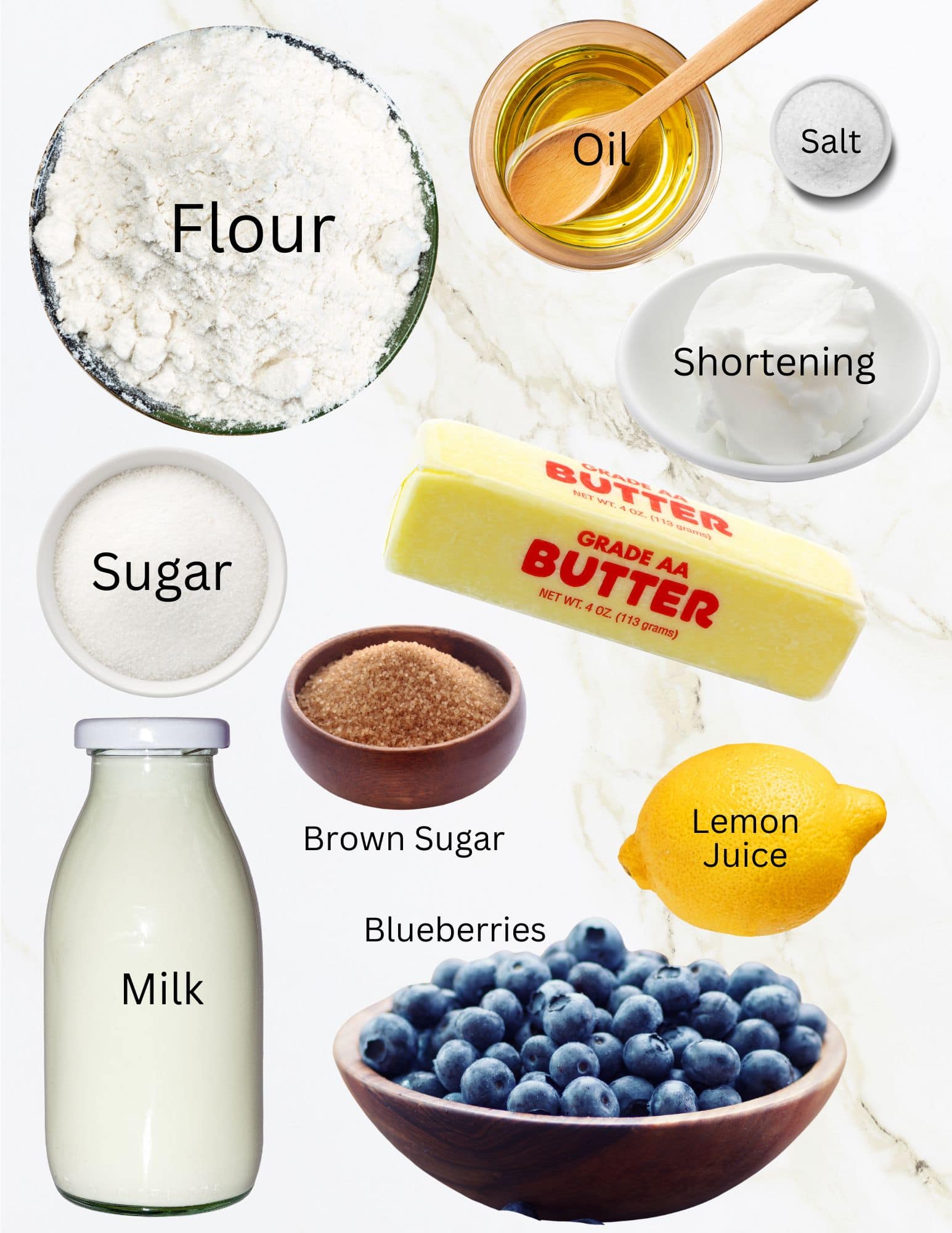 Bowls of flour, oil, salt, sugar, shortening, brown sugar and blueberries next to a lemon, stick of butter and bottle of milk.