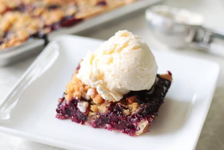 Slice of blueberry crumb slab pie with scoop of vanilla ice cream.