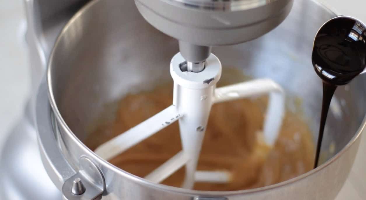 Stand mixer bowl with spoon of molasses poured into it.