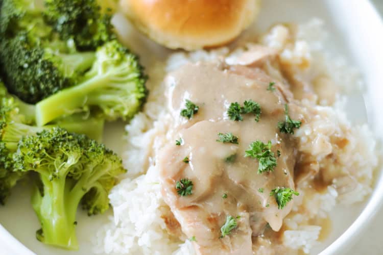 a plate with pork chops over rice, broccoli and a roll