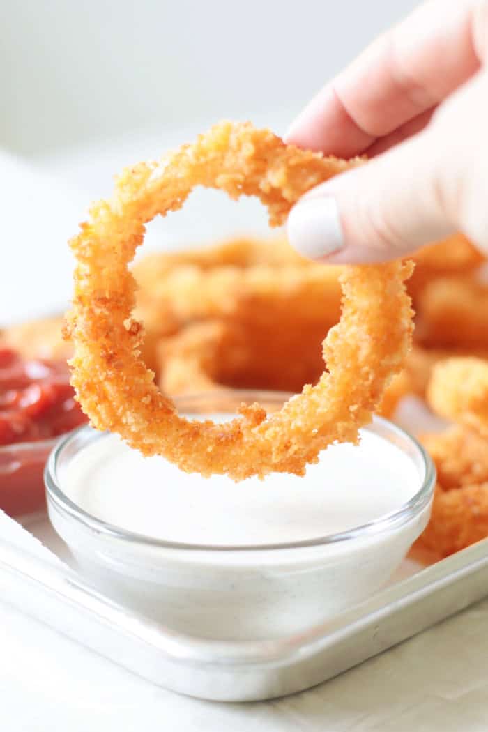 A hand holding a ring of onion rings on a tray.