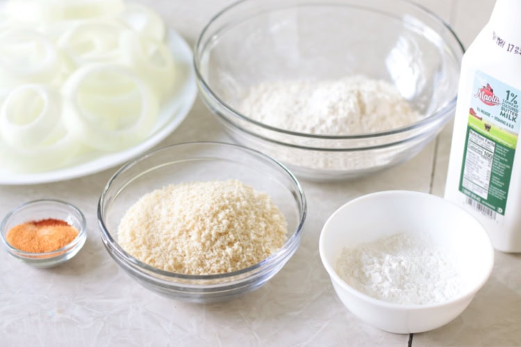 Plate of onion cut into rings, bowls of panko, corn starch, flour, and spices. Bottle of buttermilk.