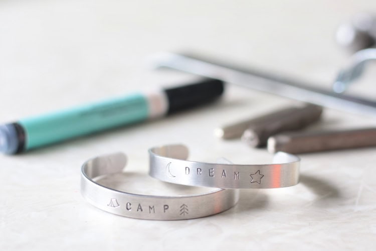 two metal stamped bracelts on table with marker and metal stamps