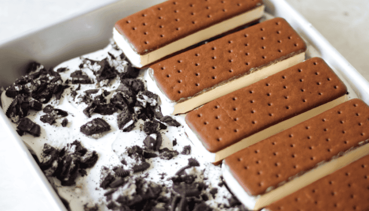ice cream sandwiches layered in metal pan with cool whip and crushed cookies