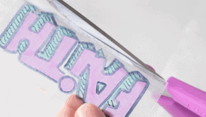 scissors cutting around edge of YW camp shrinky dink