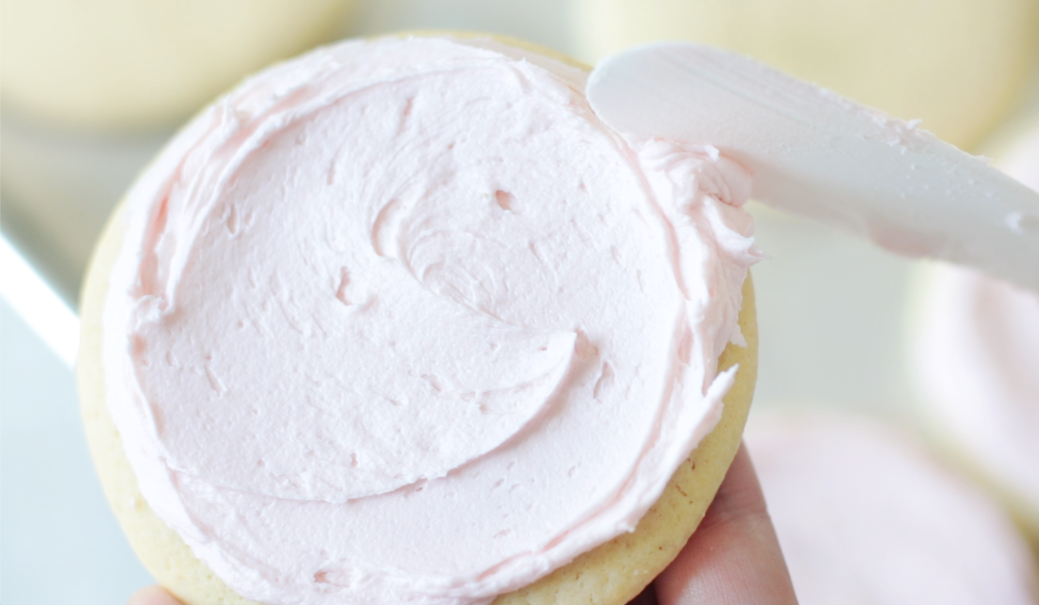 A person holding a spatula spreading frosting onto a sugar cookie