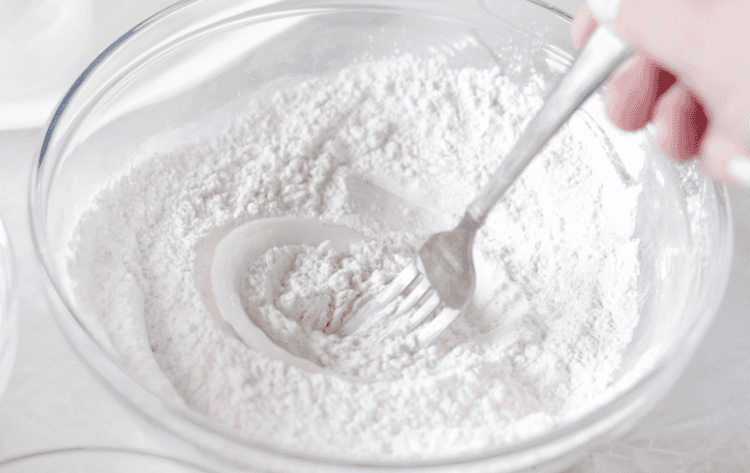 Fork dipping uncooked onion ring in flour.